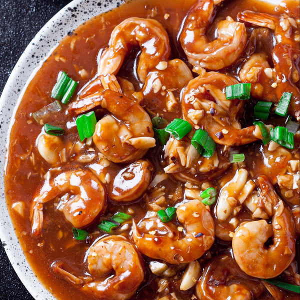 Bowl of shrimp in a rich sauce with green onions, served with white rice on a black surface.